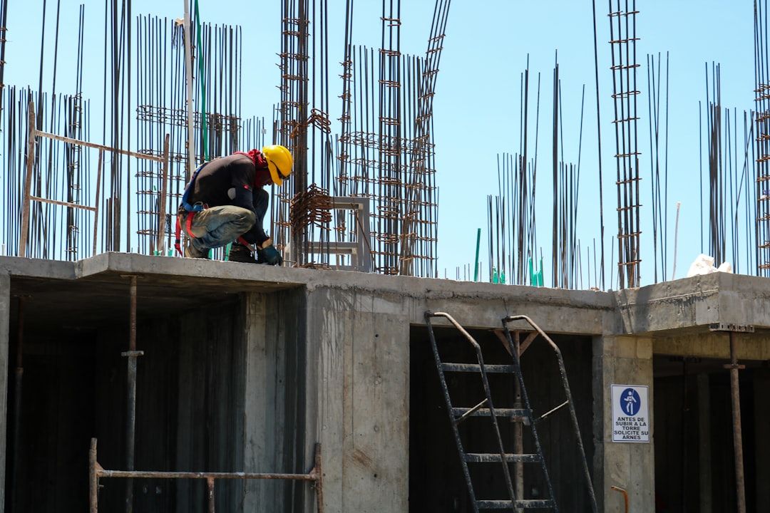 Ingenieros en un sitio de construcción analizando un modelo digital predictivo en una tableta gráfica, mostrando gráficos de reducción de costos y mapas de riesgo generados por inteligencia artificial.